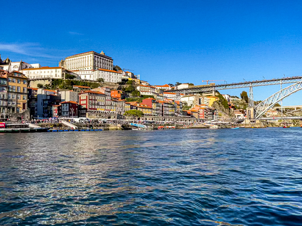 The Dom Luís I Bridge spans over the Douro River with the colorful Ribeira district in Porto, Portugal, against a clear blue sky.